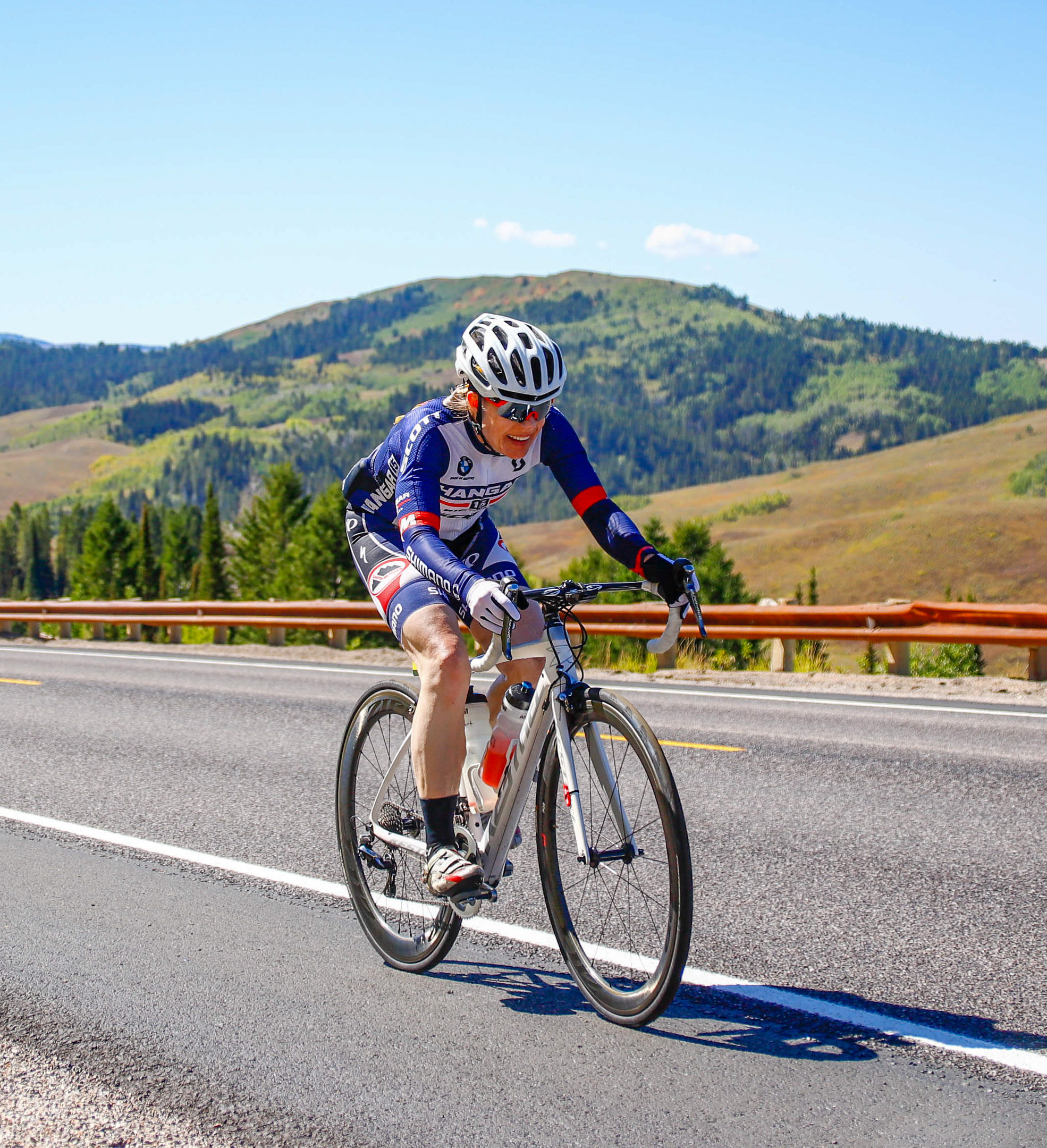Heather Albert cycling uphill at Salt Summit during the 2023 LoToJa race, with green mountains and clear blue sky in the background.